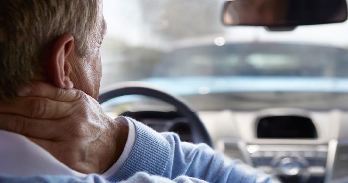 Man behind the wheel of his car, grasping his neck in pain