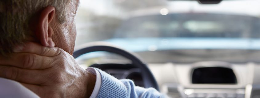 Man behind the wheel of his car, grasping his neck in pain