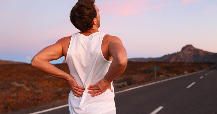 Runner grabbing his lower back with both hands, as if in pain
