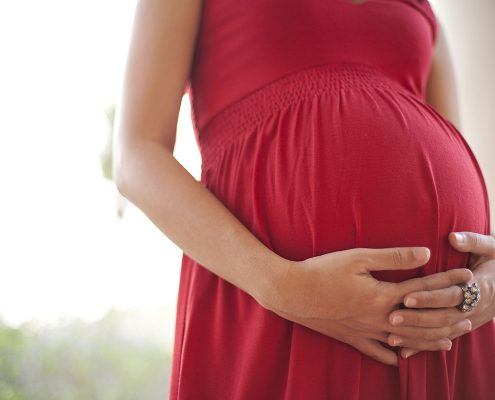 Close-up of a woman's hands clasped below her pregnant belly