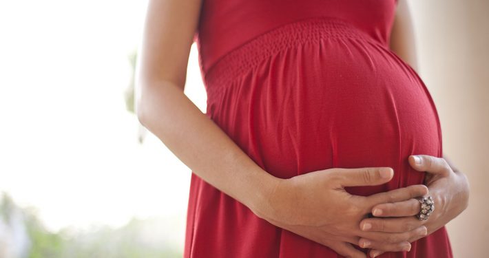 Close-up of a woman's hands clasped below her pregnant belly