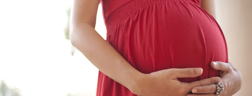 Close-up of a woman's hands clasped below her pregnant belly