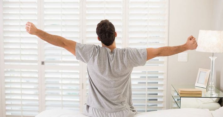 Man sitting on edge of bed, stretching, as if he's just woken up