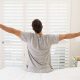 Man sitting on edge of bed, stretching, as if he's just woken up