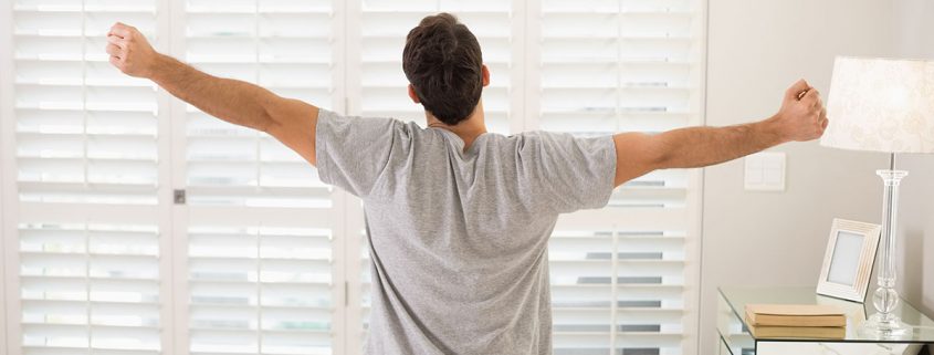 Man sitting on edge of bed, stretching, as if he's just woken up