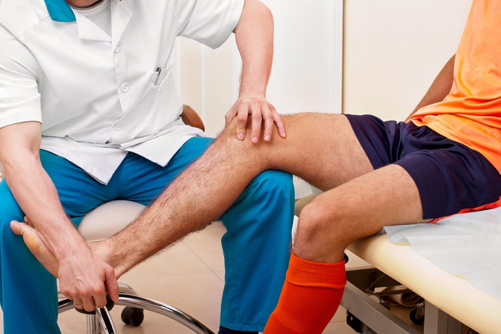 Doctor testing a knee for stability of injured football player in clinic