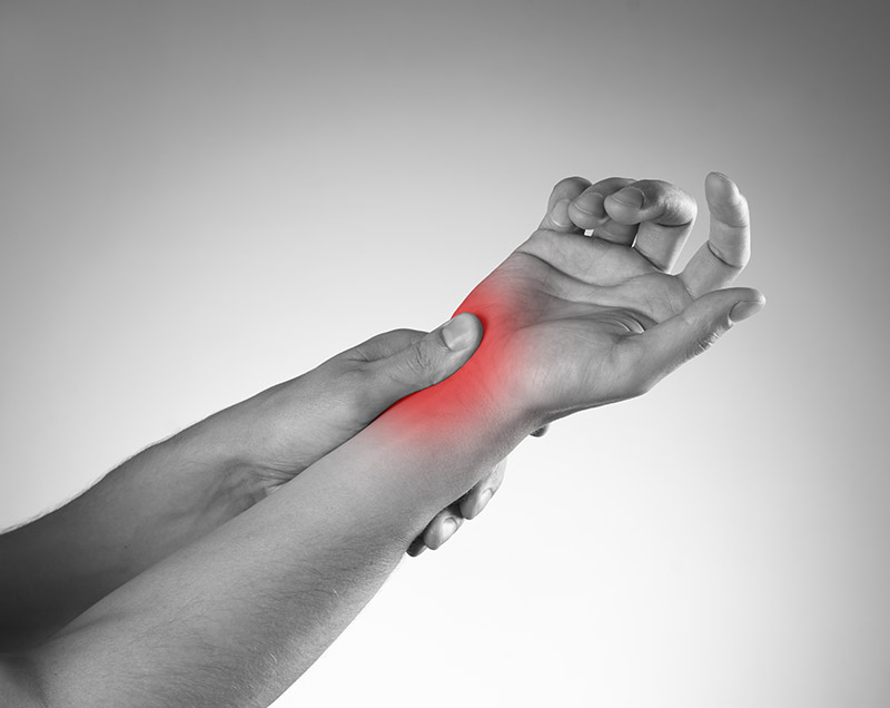 Close-up of a hand clutching a wrist, a red area added to indicate pain