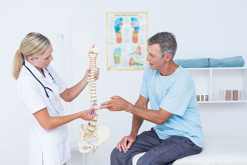 A male patient and a female medical professional consult a spinal diagram