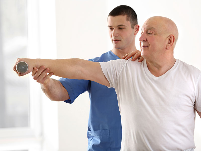 A physical therapist helps an elderly patient with strength exercises