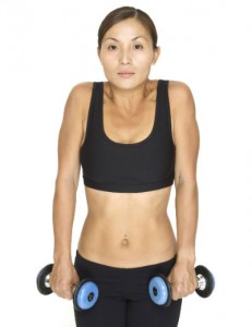 A woman holding dumbbells, her shoulders pulled up towards her ears