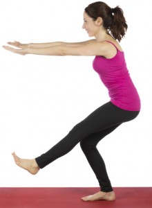 A woman in workout gear standing on her right foot, knee slightly bent, left leg straight, arms stretched forward