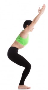 A woman in yoga gear in a half-seated position, arms stretched up