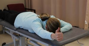 A woman lying face-down on a chiropractic table, right arm outstretched