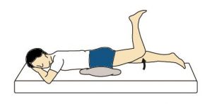 A cartoon of a man laying on his stomach, with a pillow under his hips, right leg laying flat, and left leg bent at the knee, lifting off the bed from the hip