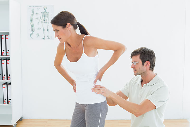 A woman wincing in pain as a male therapist examines her lower back