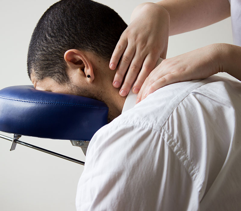 A close-up of a man in a massage chair, his neck being manipulated by a pair of hands