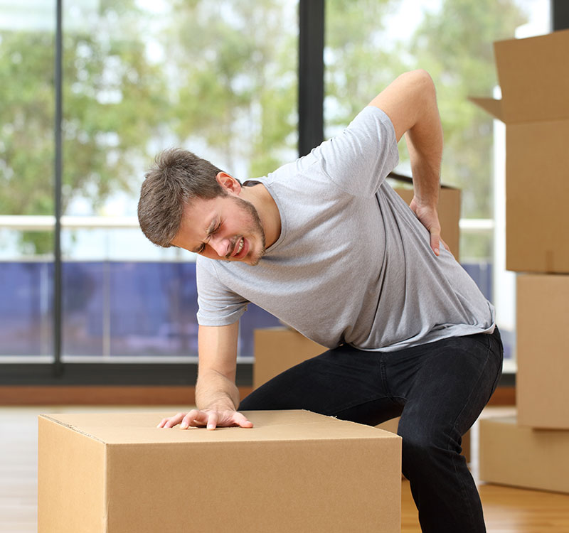 Young man moving boxes, bent over a box and grabbing his back in pain