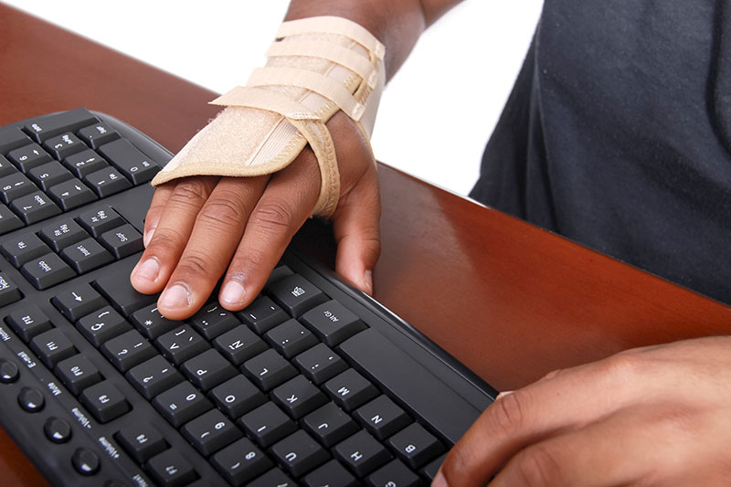 Close-up of a hand on a keyboard, a carpal tunnel brace on the wrist