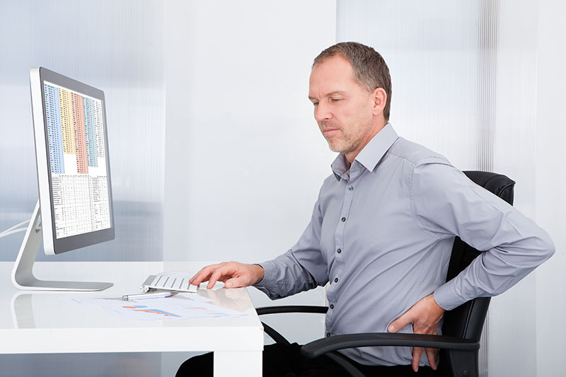 Man working at a desk, clutching his lower back as if it hurts