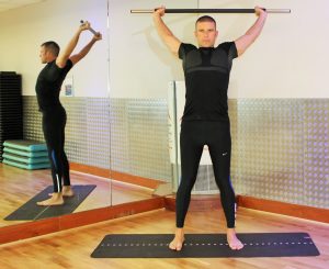 A man holding a barbell with his arms up over his head and stretched backward, as if stretching the chest