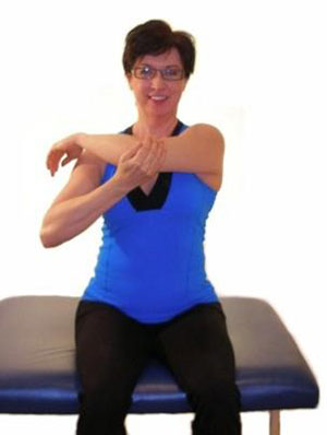 A woman sitting down, with her right hand pulling her left elbow across her chest