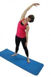 A woman in workout gear, performing a side bend with her right arm raised over her head and reaching left