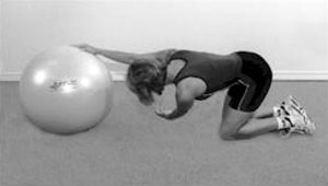 A woman, kneeling, with her right hand on an exercise ball and her left hand reaching underneath her right arm, in a trunk rotation stretch