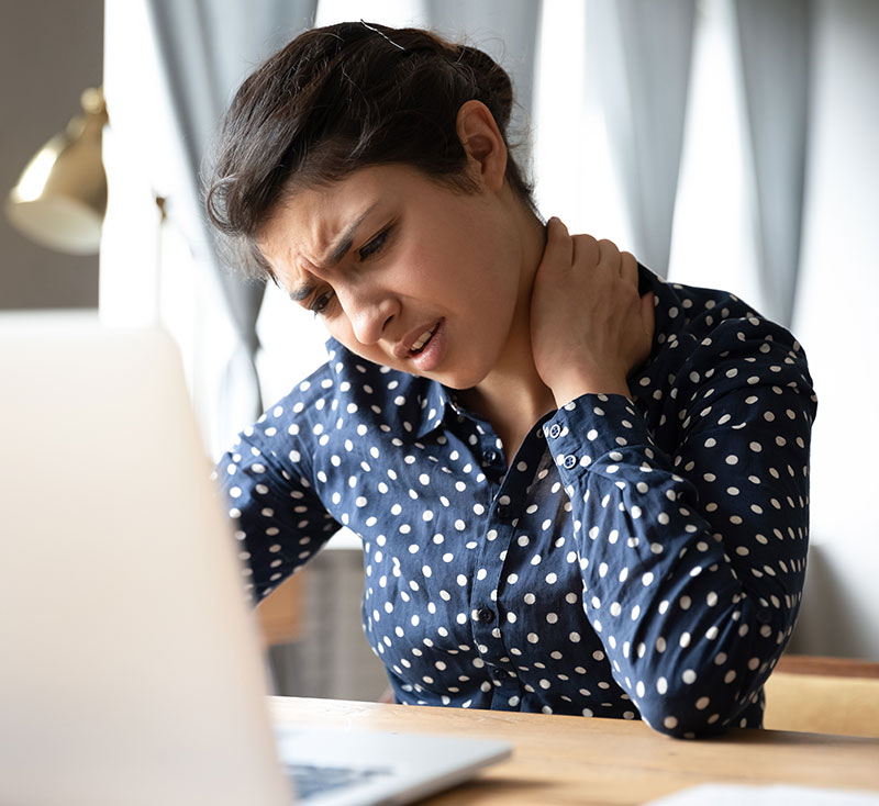 Indian ethnicity frowning woman sitting at desk in front of laptop, touch neck feels pain