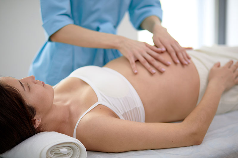Pregnant young woman with beautiful skin lying on bed having relaxing prenatal massage