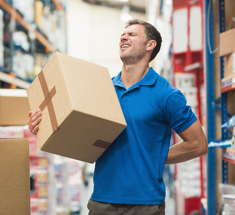 Side view of worker with backache while lifting box in the warehouse